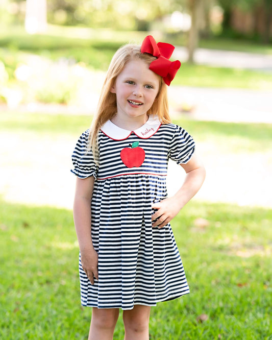 Girl wearing a navy stripe dress with an apple and a red bow on her hair 