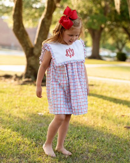 Girl wearing a red and blue windowpane dress with a red monogram