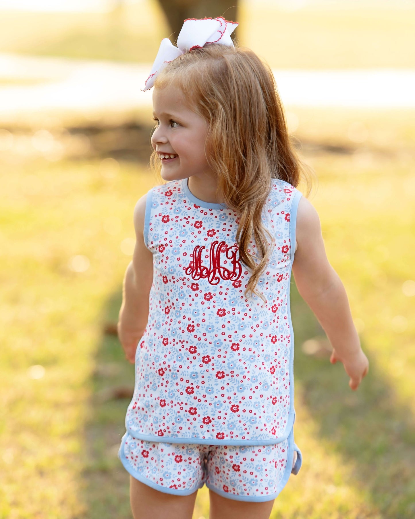 Girl wearing a red white and blue floral set with a monogram on the chest. Smiling looking away