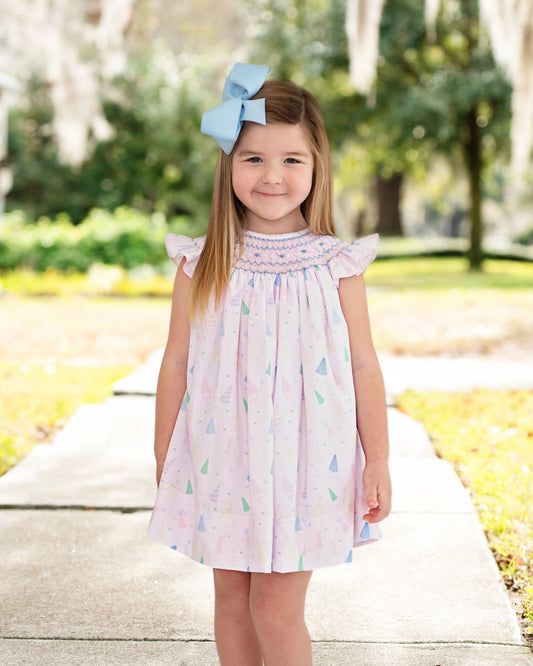 Girl wearing birthday print dress with smocking details and a blue bow on her hair 