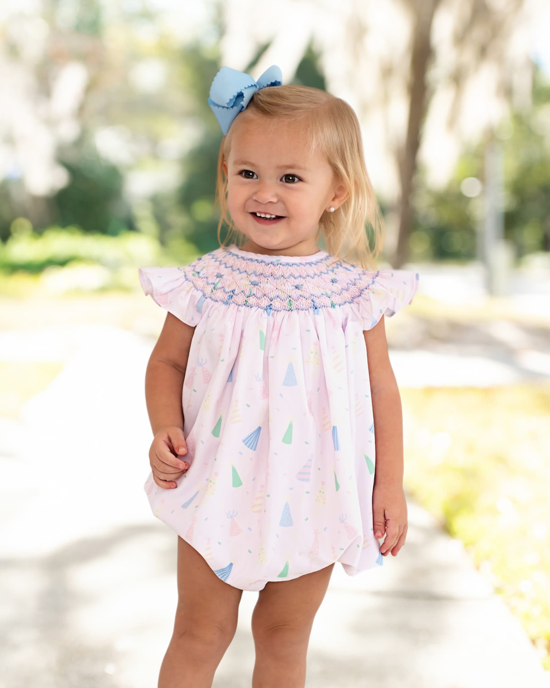 Girl wearing party hat print outfit with a blue bow on her hair smiling