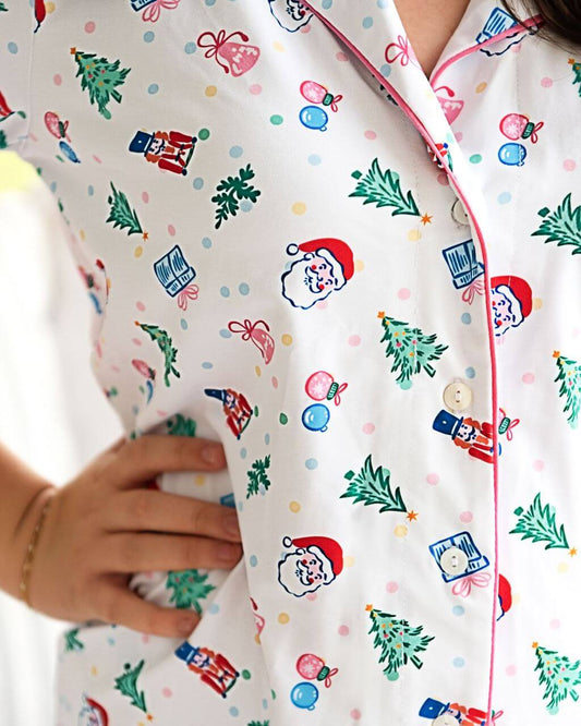 Girls Christmas pajamas featuring a fun holiday print with Santa, Christmas trees, nutcrackers, and ornaments. Soft, breathable fabric with button-front styling and pink piping for a festive, comfortable look all season long.