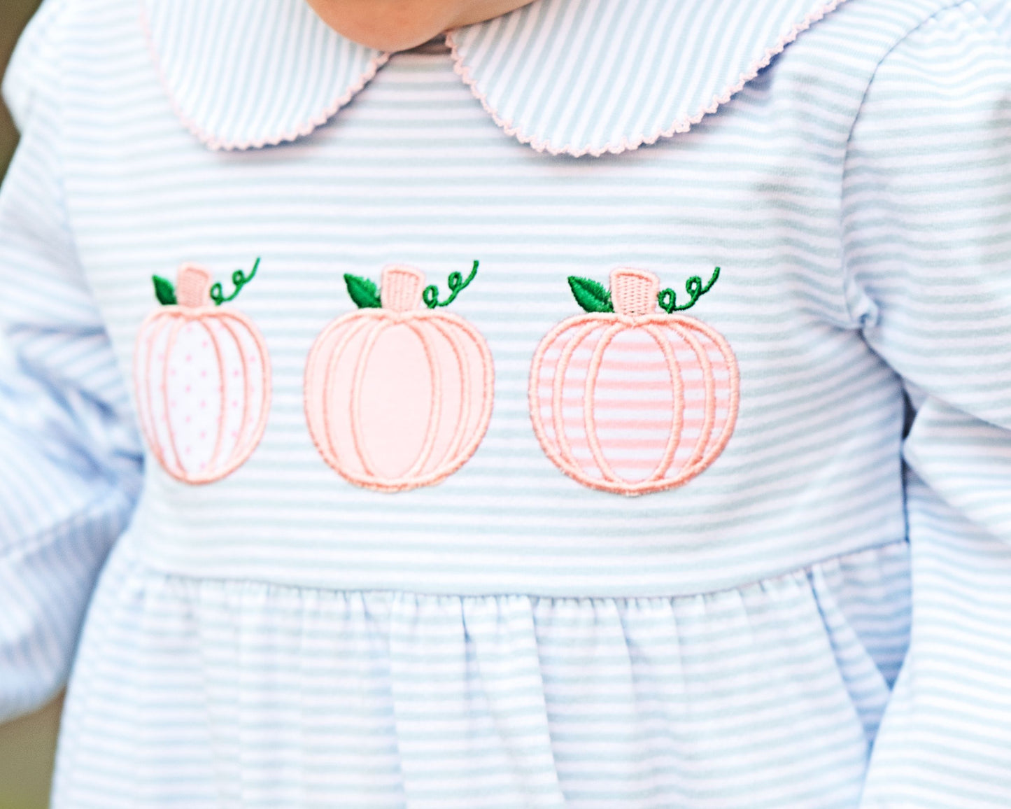 Light blue and white striped dress with pink pumpkins and green leaves on a blurred background