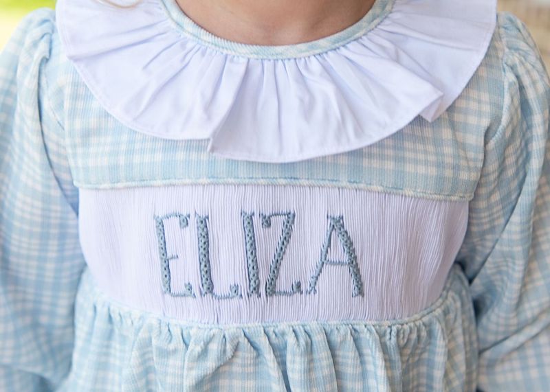 Light blue checkered dress with white collar and embroidered name 'Eliza' on a white background