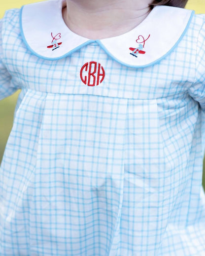 Light blue checkered dress with white collar featuring red monogram, on a yellow background.