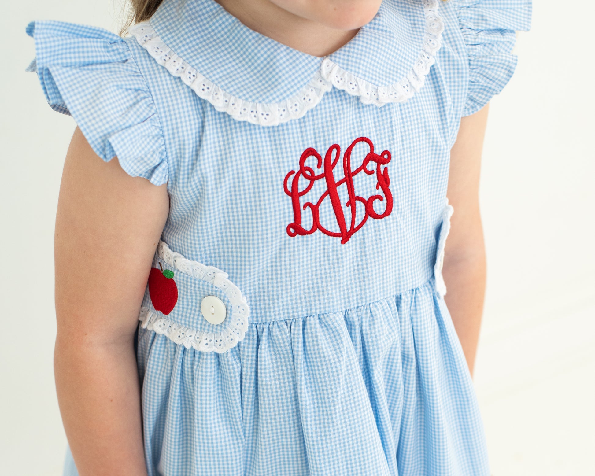Light blue checkered dress with white lace collar and red monogram on a plain background