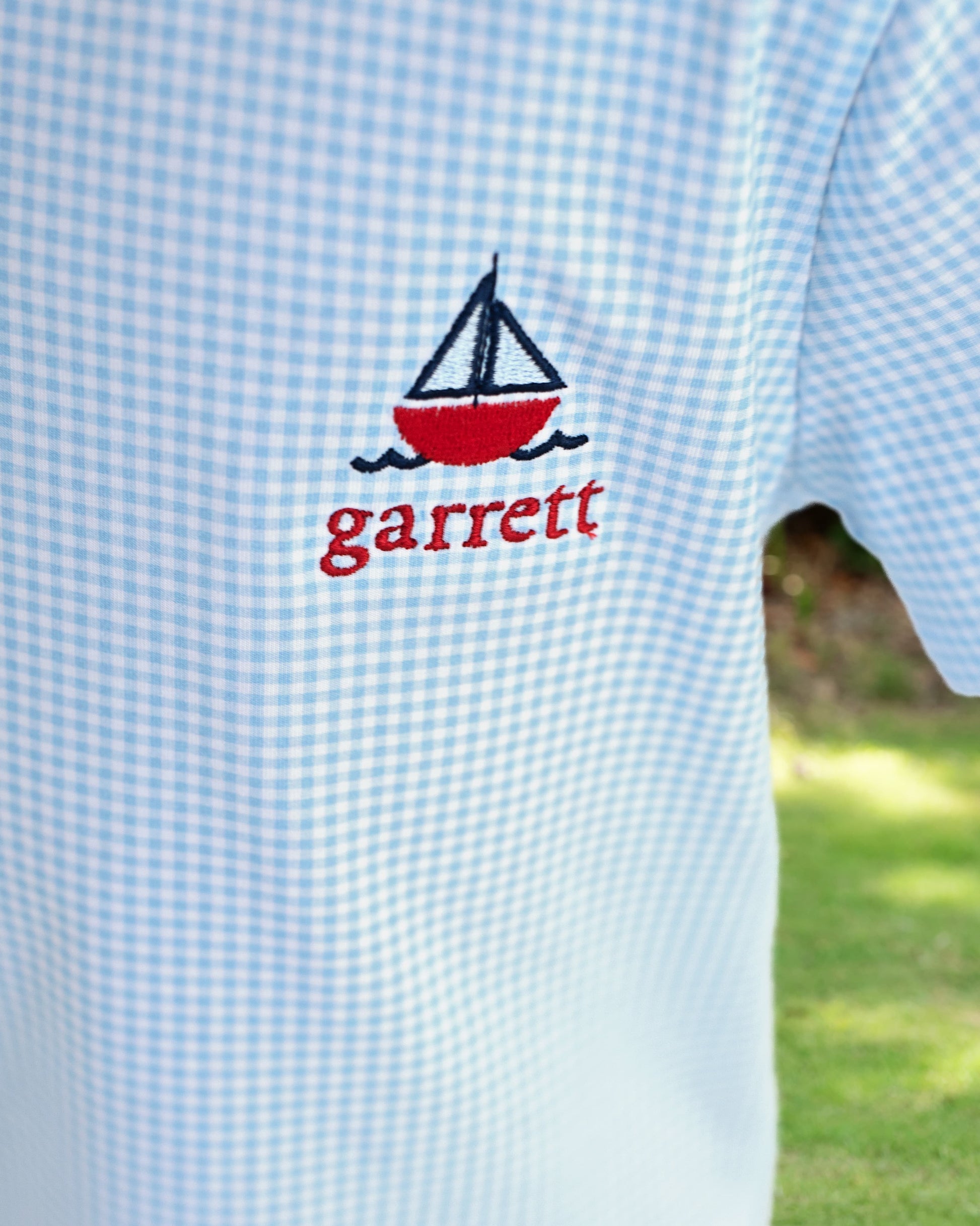 Light blue checkered shirt with a red sailboat design and 'garrett' monogram.