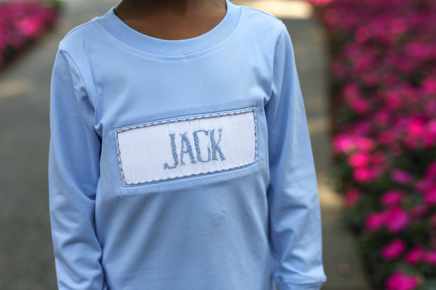 Light blue long-sleeve shirt with 'JACK' on a blurred floral background