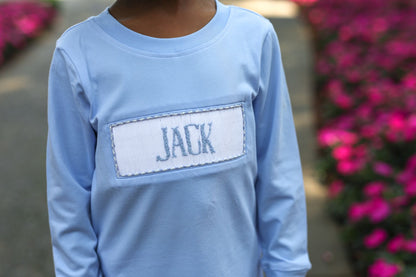 Light blue long-sleeve shirt with 'JACK' on a blurred floral background