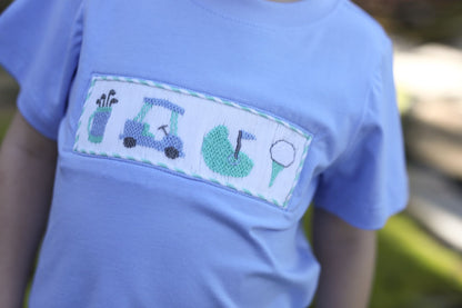 Light blue t-shirt with golf-themed design on a blurred outdoor background