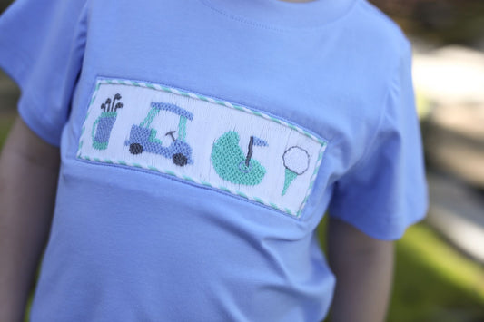 Light blue t-shirt with golf-themed design on a blurred outdoor background