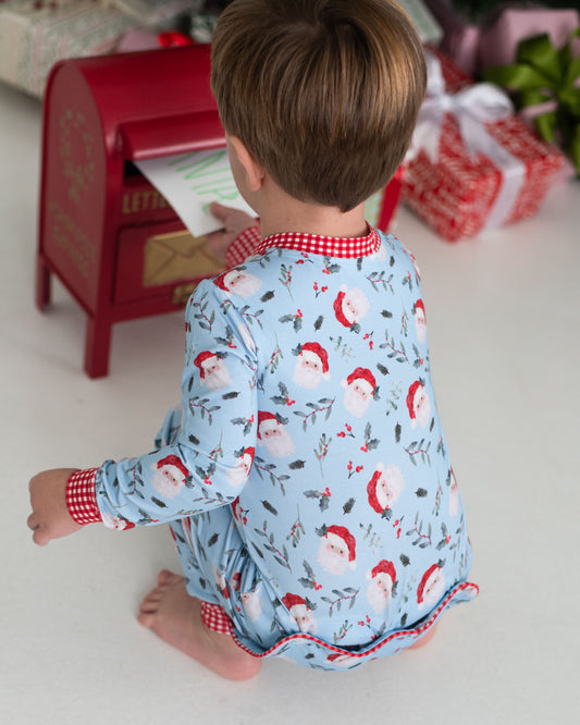 Little boy wearing holiday pajamas putting a letter to Santa into a mailbox
