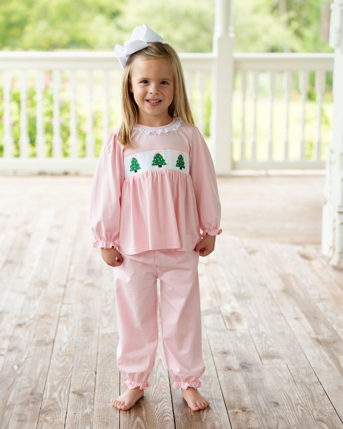Little girl standing outside wearing a Pink Knit Smocked Christmas Tree Pant Set