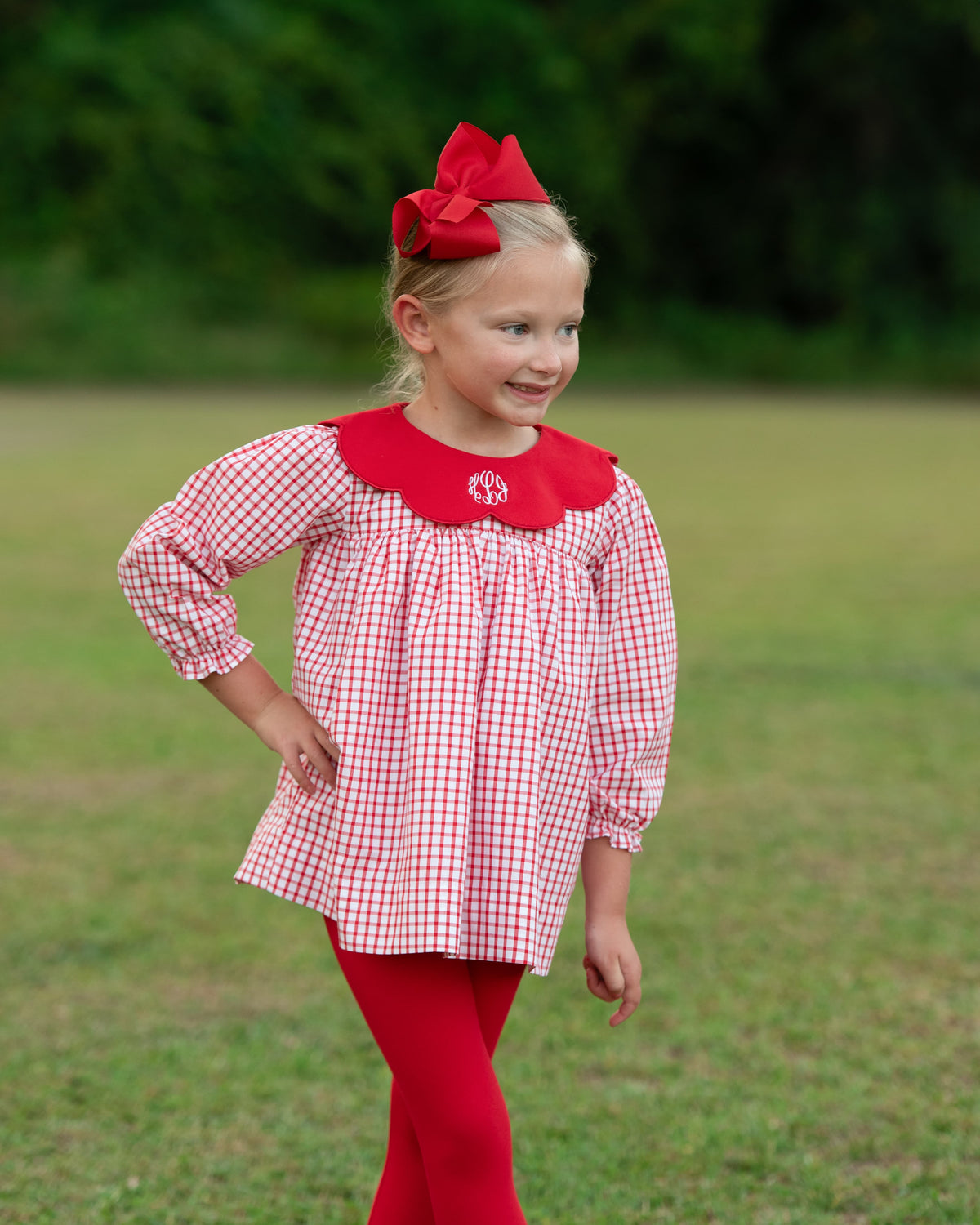 Little girl standing outside wearing a red and white windowpane top and matching red leggings and a red bow in her hair