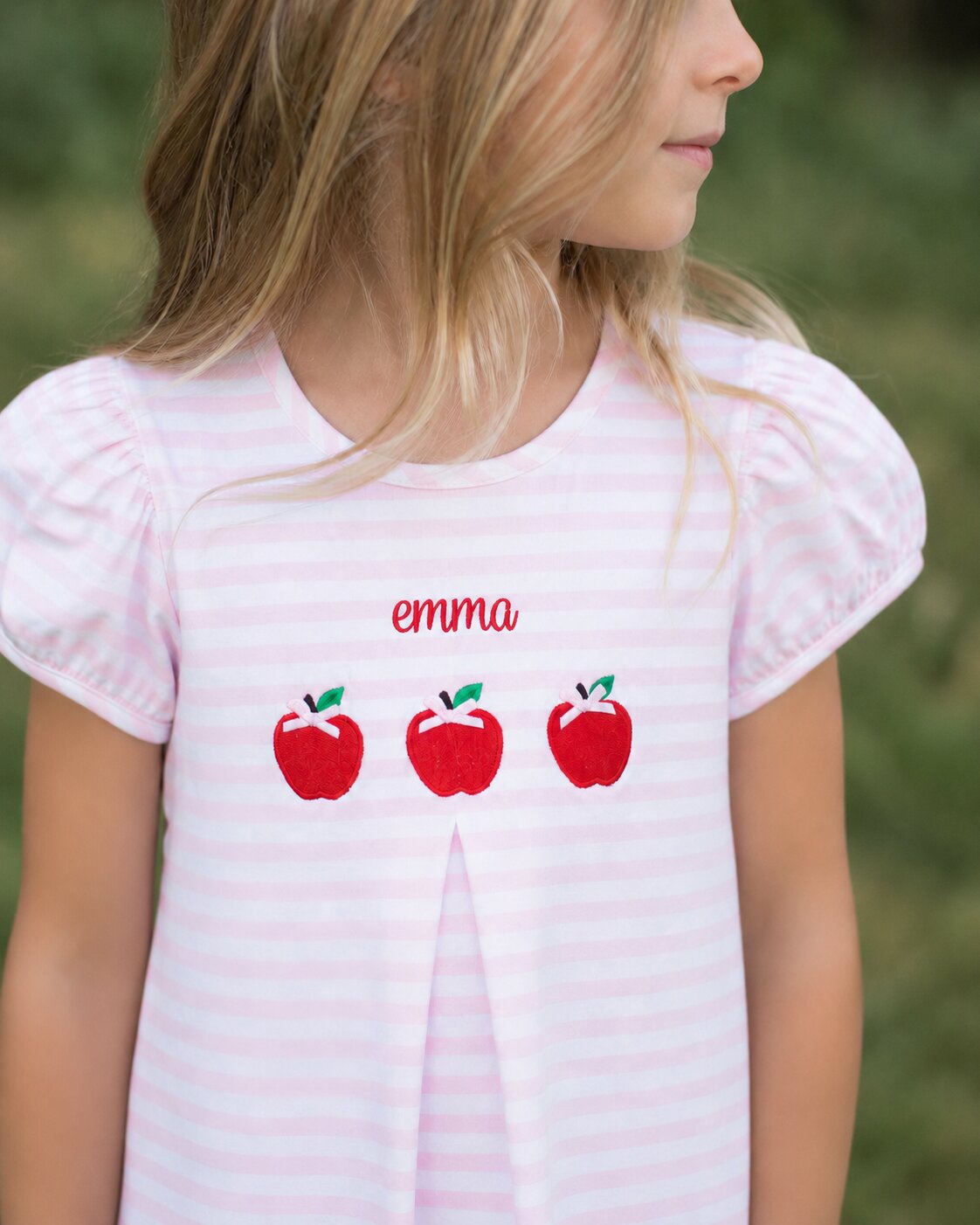Little girl wearing a pink striped dress with applique apples and a monogram