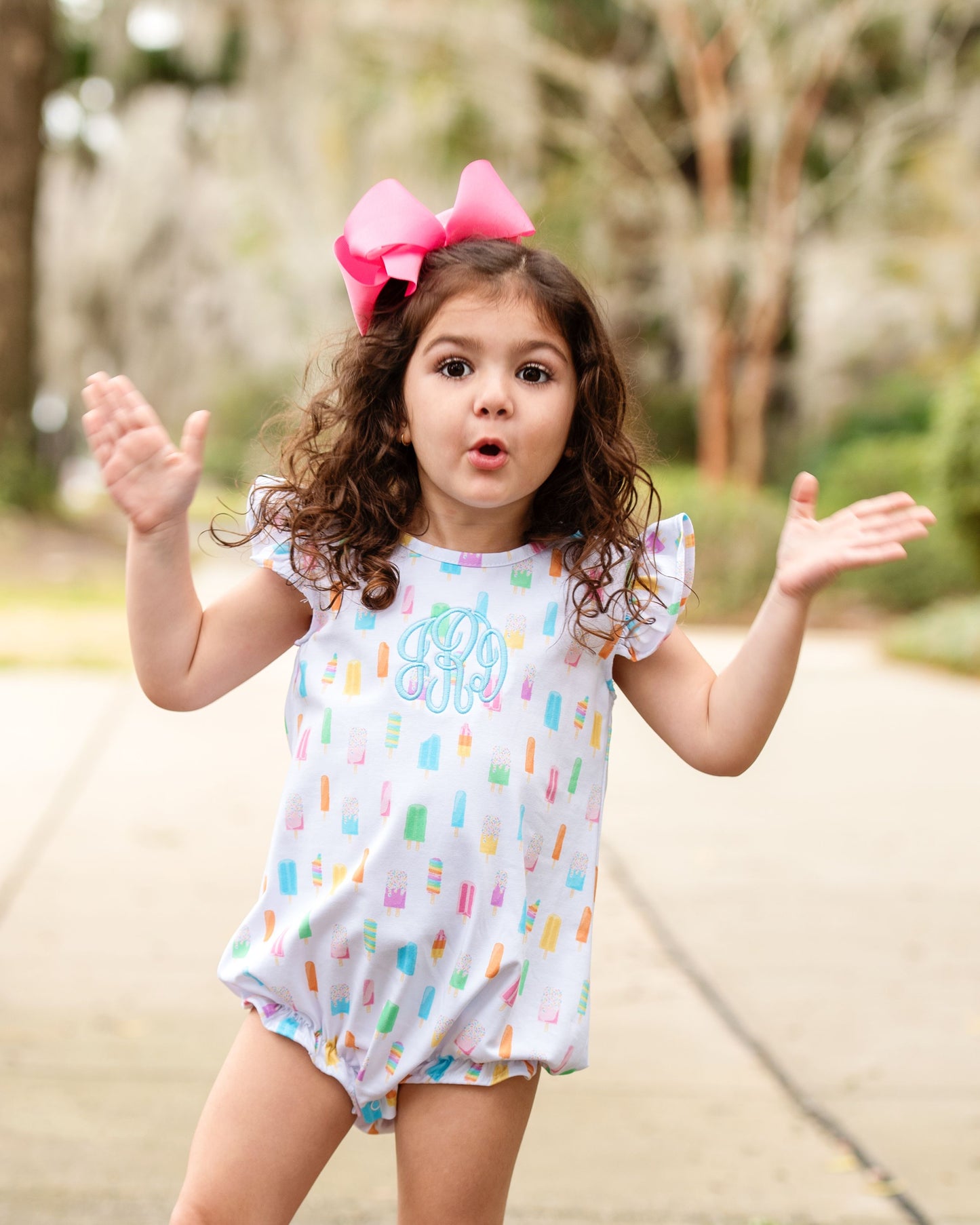 Little girl wearing a popsicle print bubble outside with a pink bow in her hair