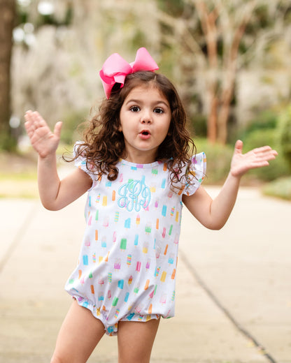 Little girl wearing a popsicle print bubble outside with a pink bow in her hair