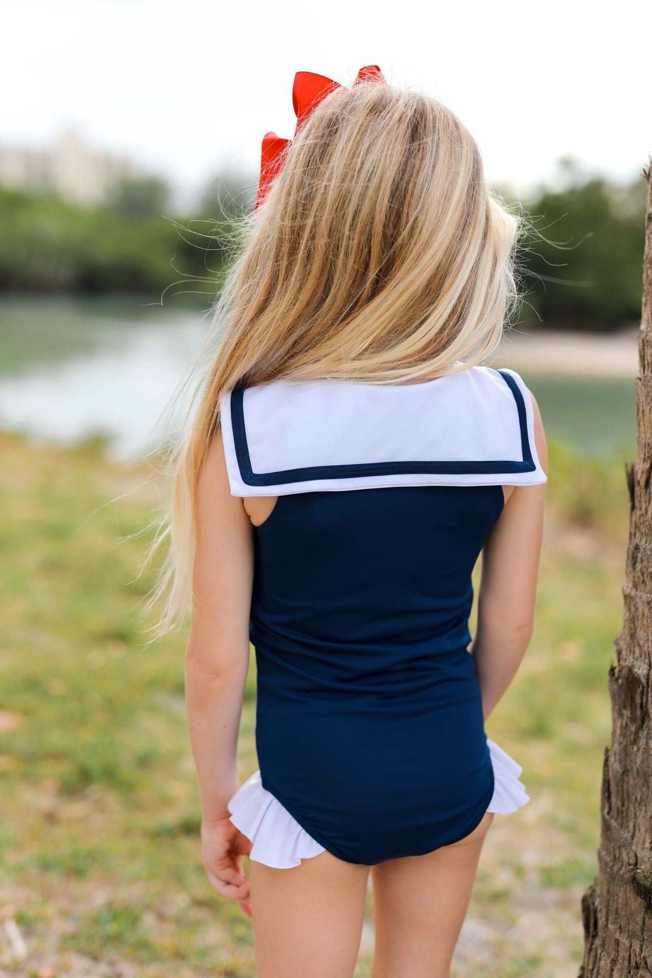 Person wearing a navy blue and white sailor-style swimsuit with a red bow in a natural setting.
