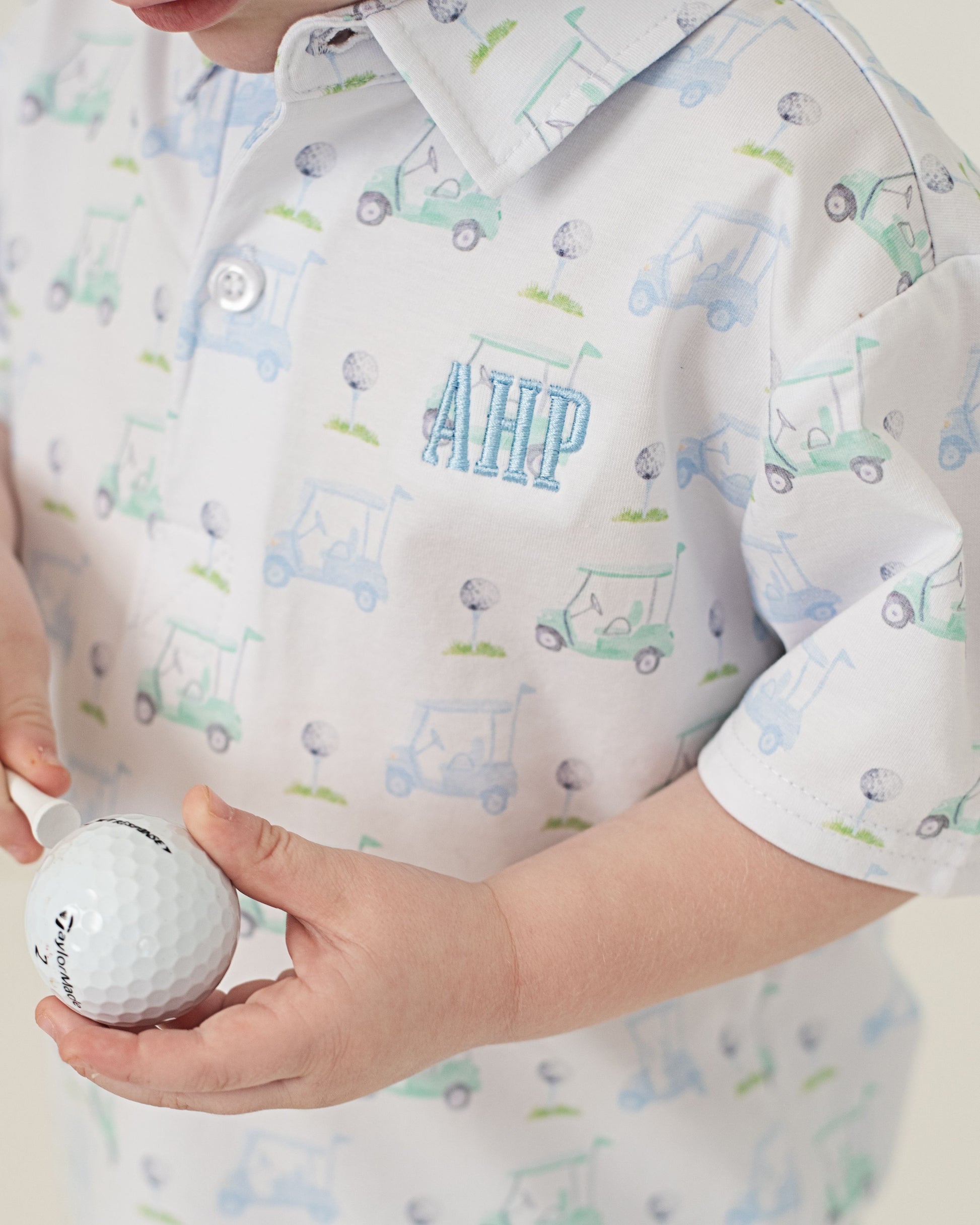 Person wearing a shirt with car patterns holding a golf ball.