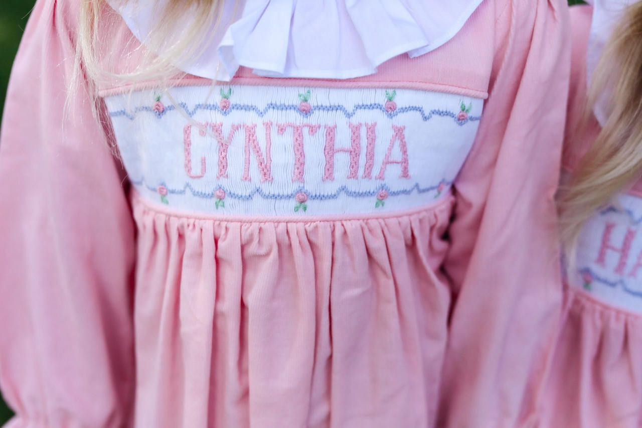 Pink dress with embroidered name 'Cynthia' on a white background