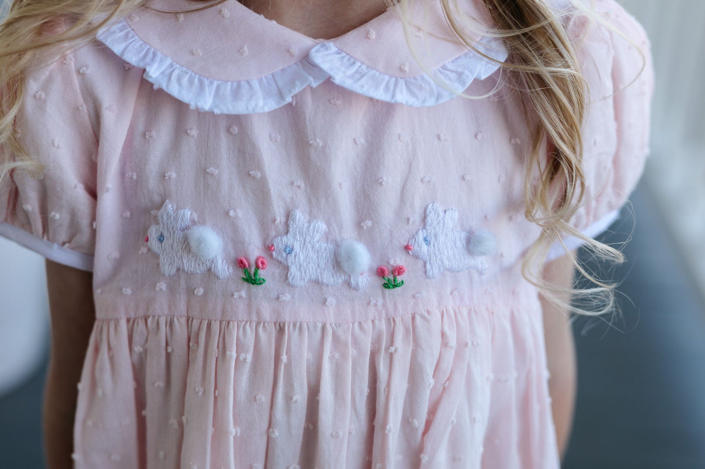 Pink dress with white ruffled collar and embroidered bunny design on a blurred background