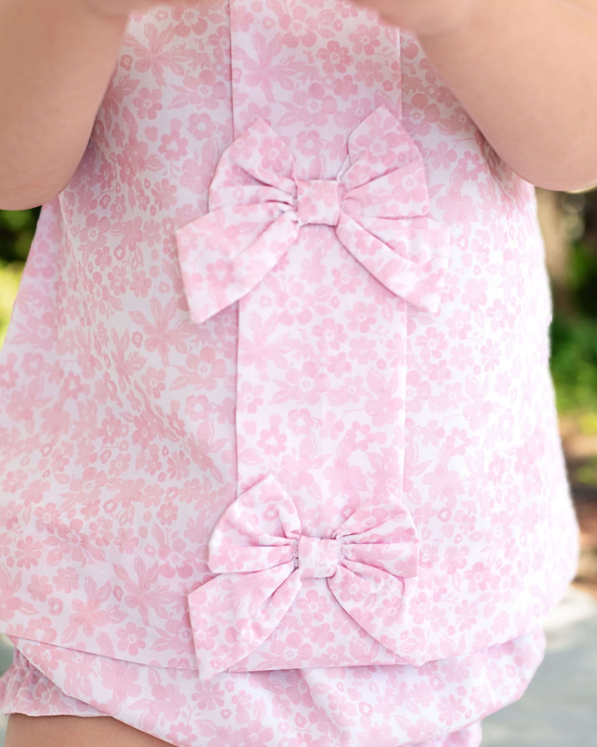 Pink floral dress with a large bow on a blurred natural background