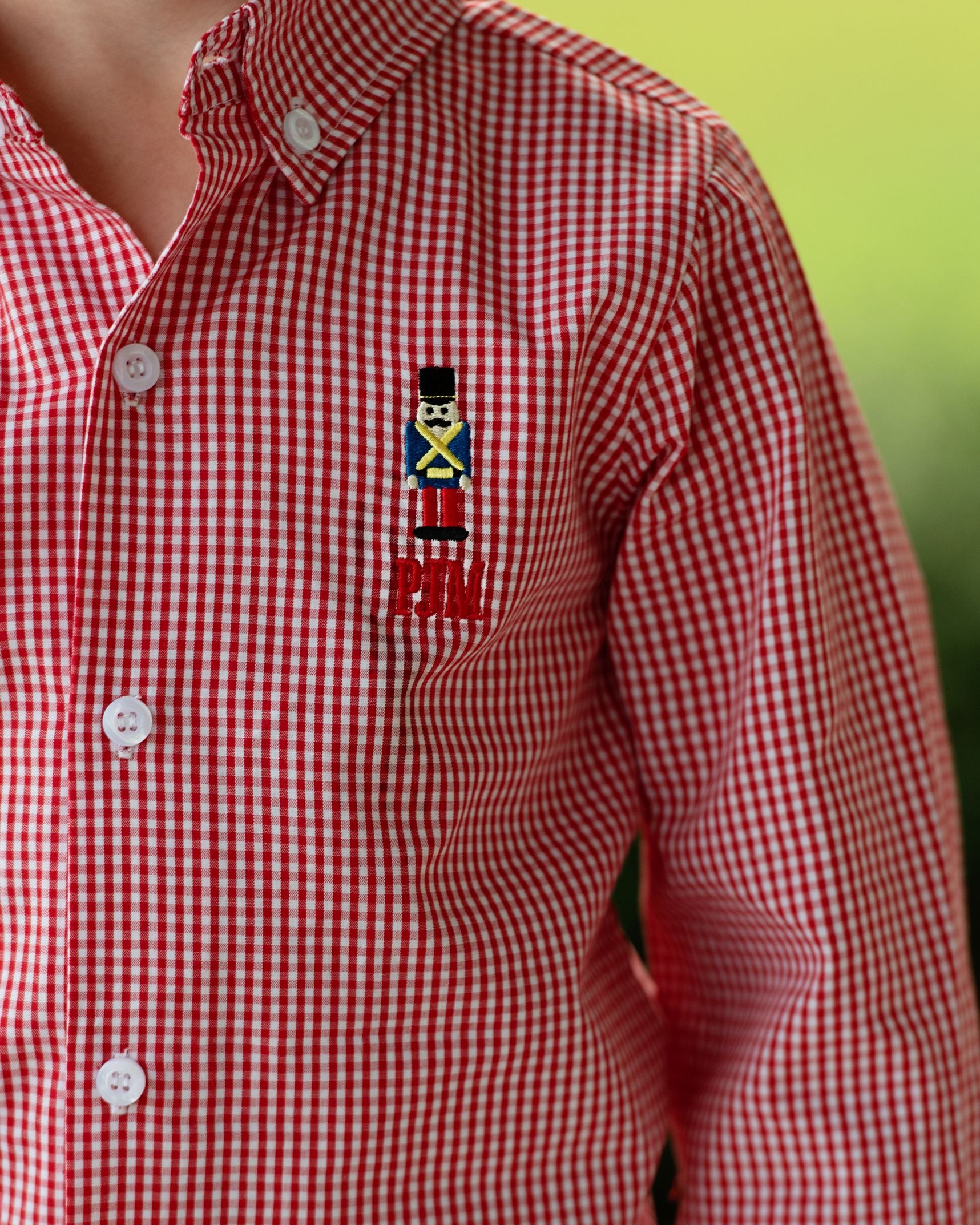 Red and white checkered shirt with a embroidered design on a blurred green background