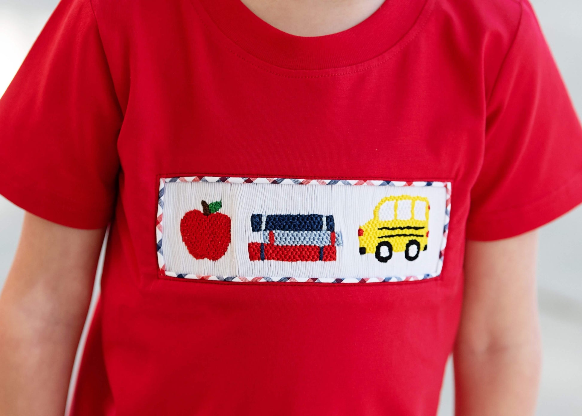 Red t-shirt with a pocket featuring an apple, car, and school bus design.