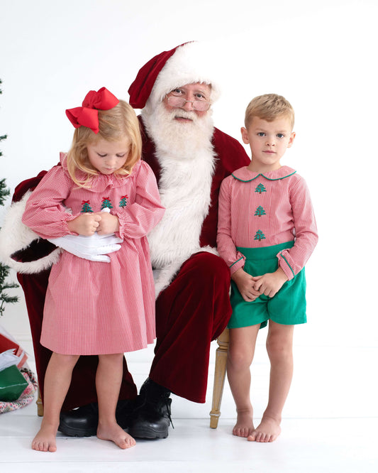 Santa Claus sitting with two children in festive outfits on a white background