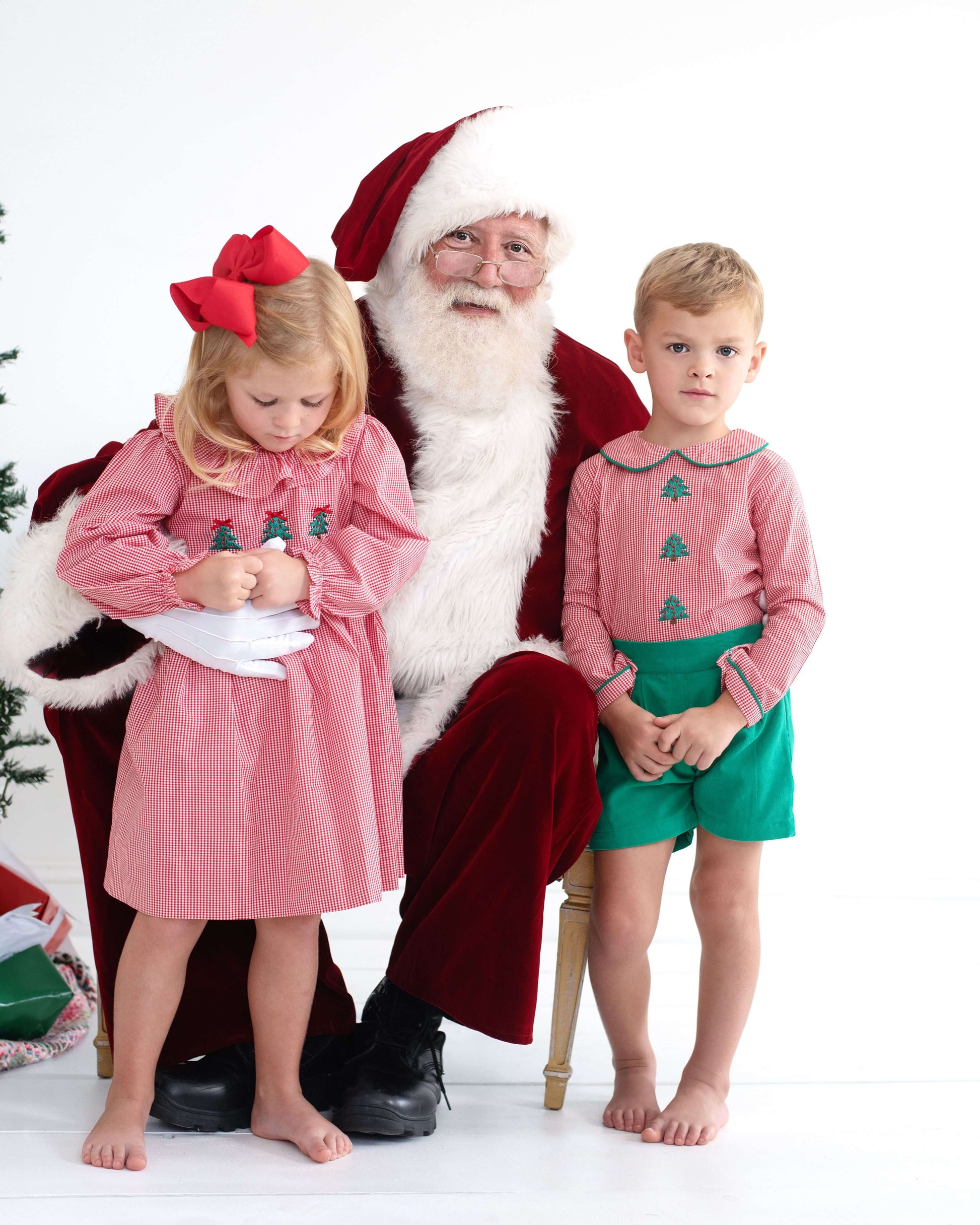 Santa Claus sitting with two children in festive outfits on a white background