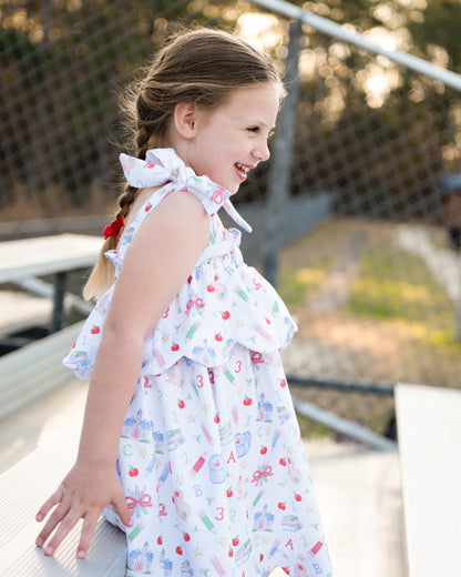 Sideview of a young girl standing by bleachers wearing a school themed dress.
