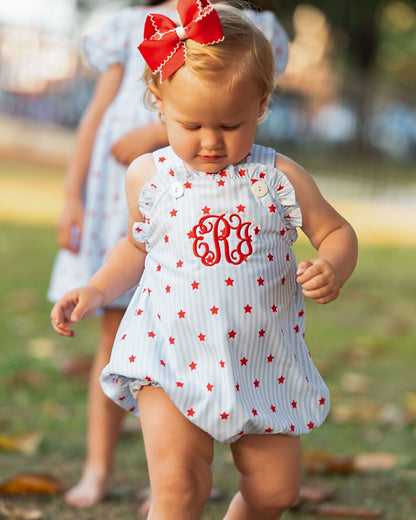 Small child wearing a star print outfit with a monogram on the chest and a red bow on her hair.