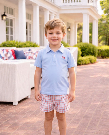 Smiling boy wearing a blue polo shirt and plaid shorts.