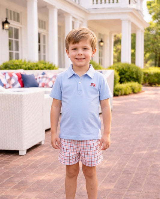 Smiling boy wearing a blue polo shirt and plaid shorts.