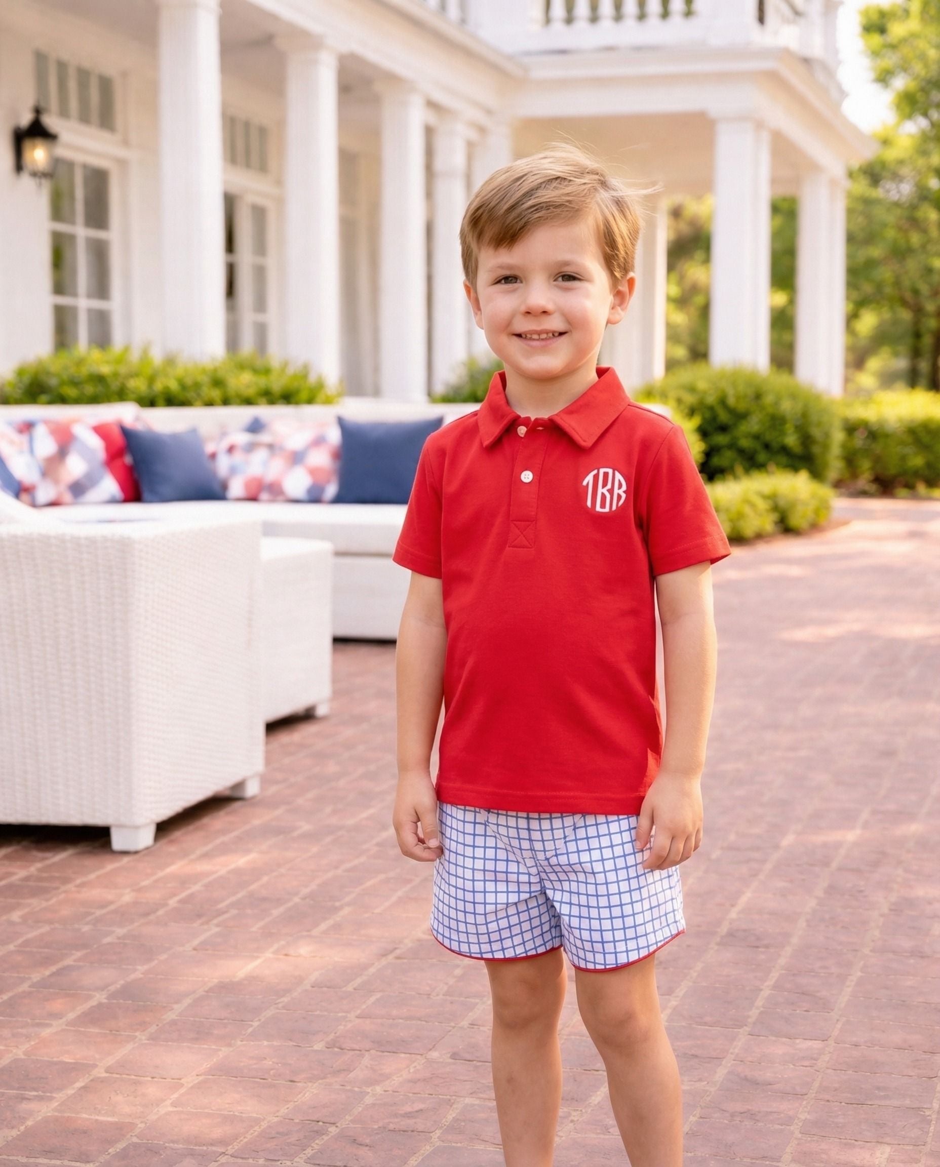 Smiling boy wearing a red polo shirt and blue windowpane shorts.