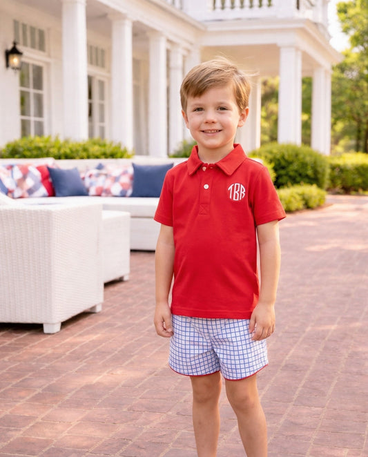 Smiling boy wearing a red polo shirt and blue windowpane shorts.