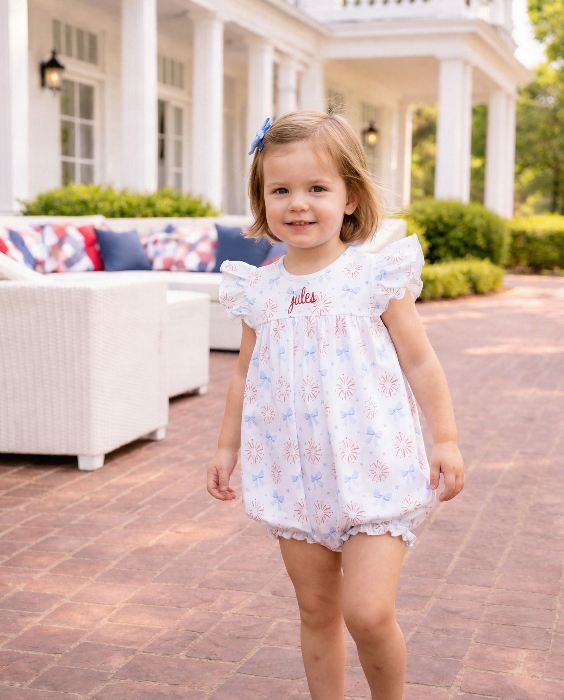 Smiling girl in firework and bow print outfit with the name jules embroidered. 