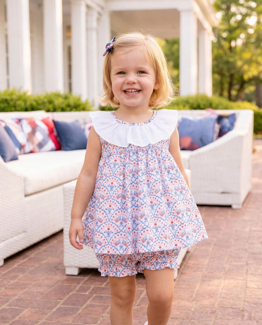 Smiling girl in flag print outfit standing in front of an outdoor sitting set. 