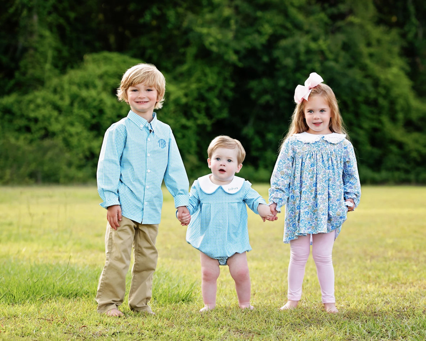 Three children holding hands in a field with greenery in the background