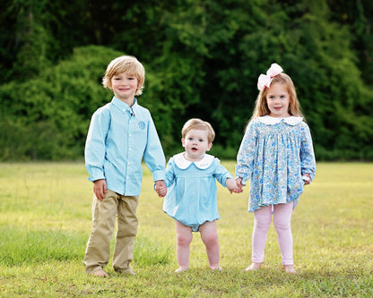 Three children holding hands in a field with greenery in the background