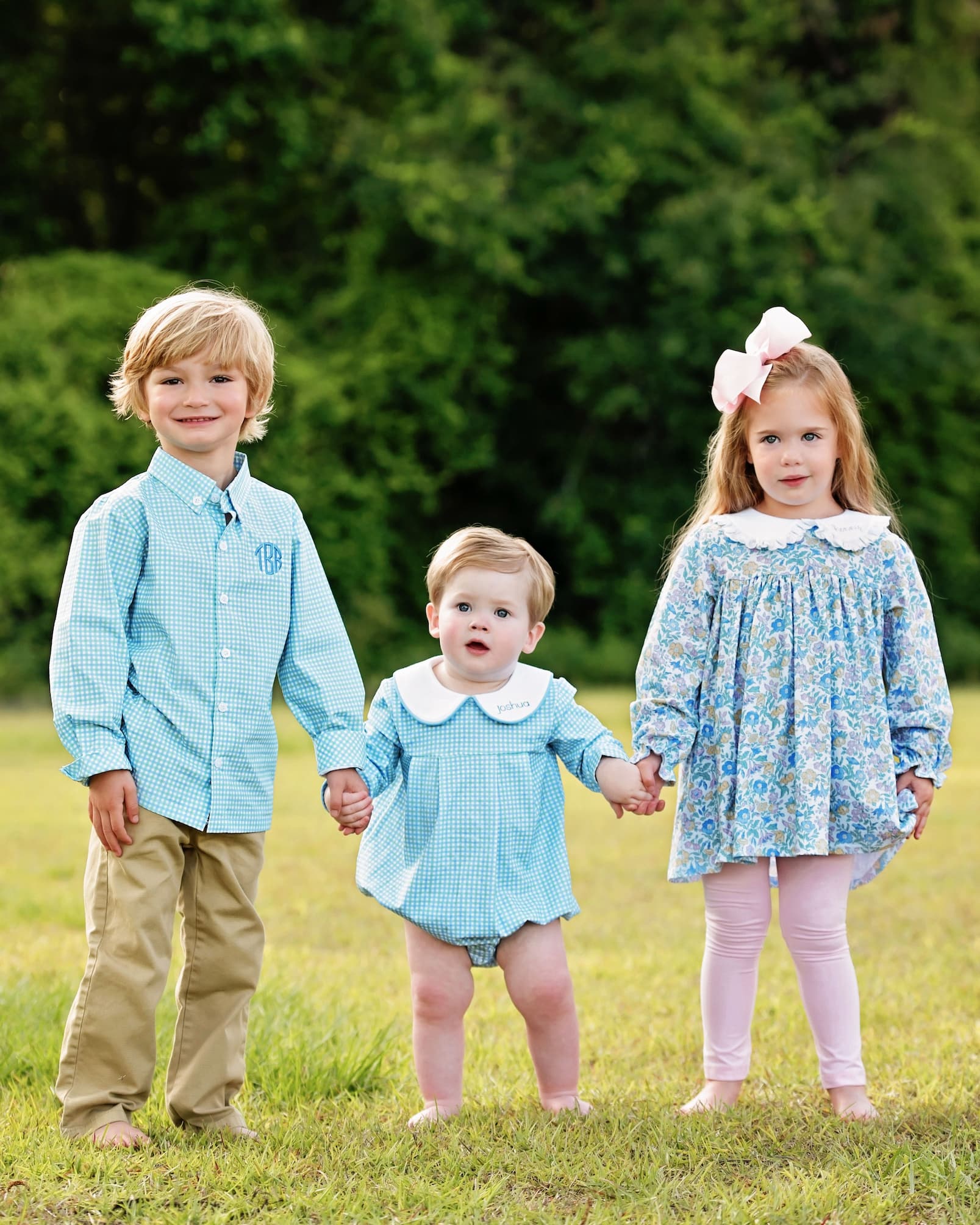 Three children holding hands in a grassy field with a blurred green background
