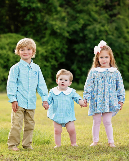 Three children holding hands in a grassy field with a blurred green background