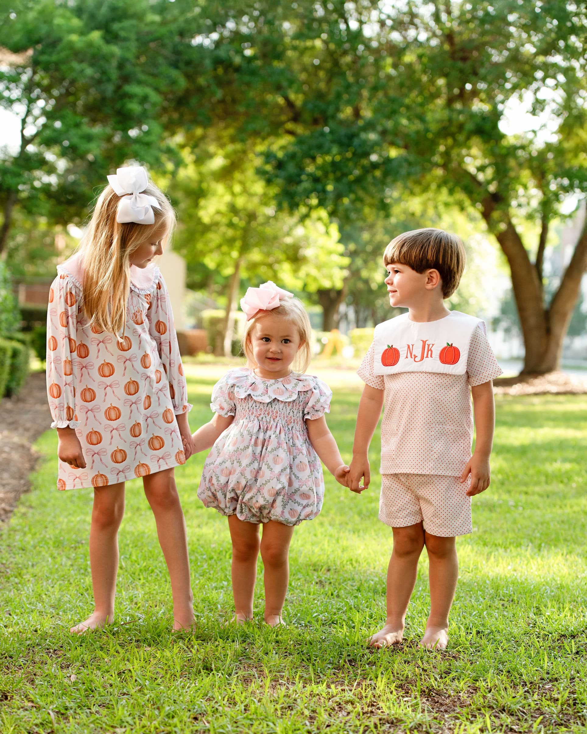 Three children holding hands in a park with greenery in the background