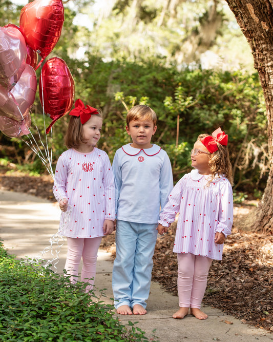 Three children in Valentine outfits with red bows outdoors, holding balloons.