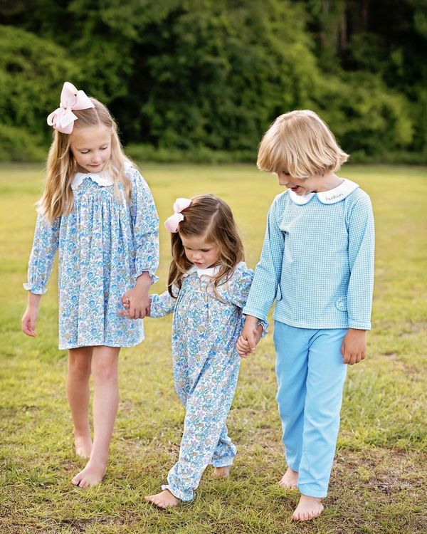 Three children in matching blue outfits standing in a grassy field.