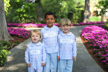 Three children in matching outfits standing on a path with pink flowers and greenery in the background
