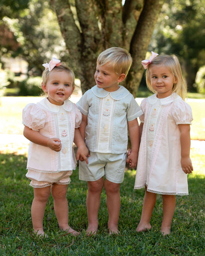 Three children in matching outfits standing on grass with trees in the background