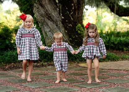 Three children in matching plaid outfits walking hand-in-hand on a stone path.