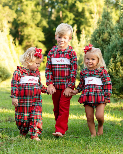 Three children in matching red plaid outfits standing outdoors with trees in the background.