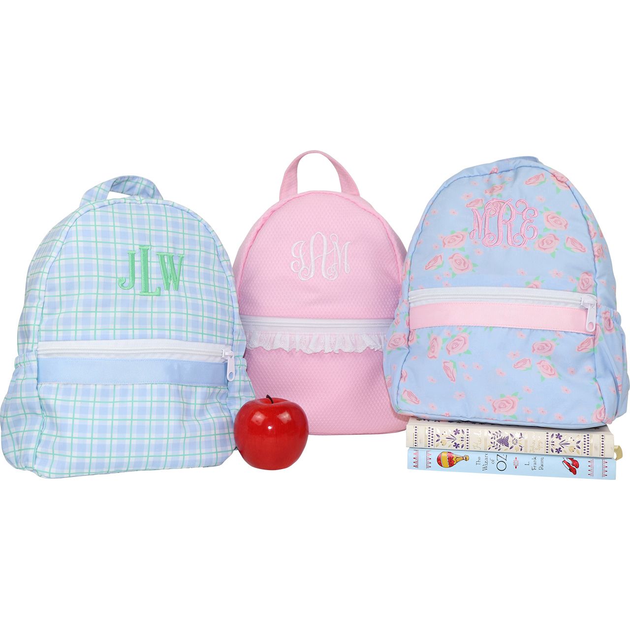 Three children's backpacks with monograms and a red apple on a white background